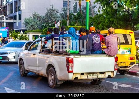 Camioncino sovraccarico con operai seduti sul cassone aperto che percorre una strada thailandese tropicale con palme e ambiente urbano visibile Foto Stock