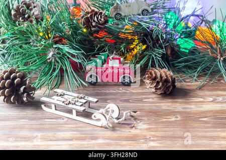 Slitta giocattolo di legno e camioncino giocattolo rosso con testo "Buon Natale" su un tavolo di legno con rami di pino Foto Stock