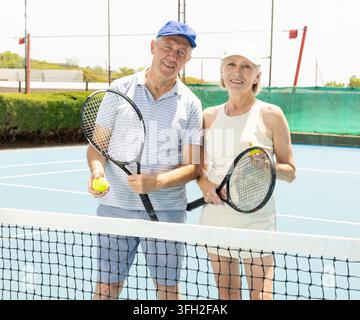 Ritratto di una coppia di anziani sorridenti con racchette da tennis su un campo da tennis. Concetto di pensionamento e stile di vita attivo per anziani. Foto Stock
