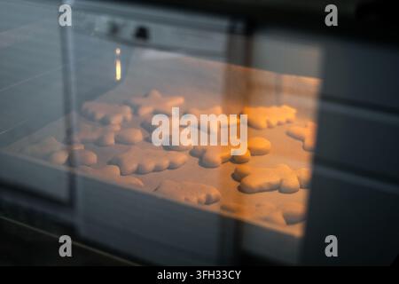 Biscotti di Natale in forme festive che cuociono su una teglia dentro un forno caldo, visti attraverso la porta del forno. Foto Stock