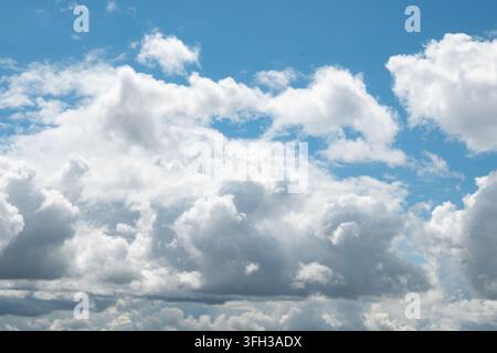 Una vista orizzontale luminosa di nuvole bianche e soffici contro un cielo azzurro chiaro. La luce naturale soffusa illumina gli strati testurizzati delle nuvole in Foto Stock