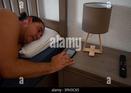 Uomo sdraiato a letto, che usa il suo smartphone al mattino Foto Stock