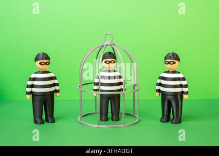 Uno dei tre criminali seduti in una gabbia. Statistiche di rilevamento dei reati. Ricerca di complici. Concetto di applicazione della legge e investigazione criminale Foto Stock