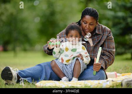Madre nera che soffia bolle di sapone con la figlia nel parco Foto Stock