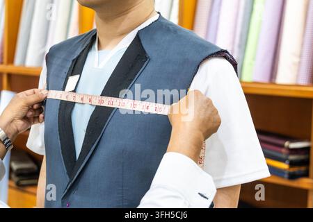Primo piano di un sarto professionista che misura il corpo del cliente con un metro per assicurarsi che la giacca del completo sia ben aderente Foto Stock