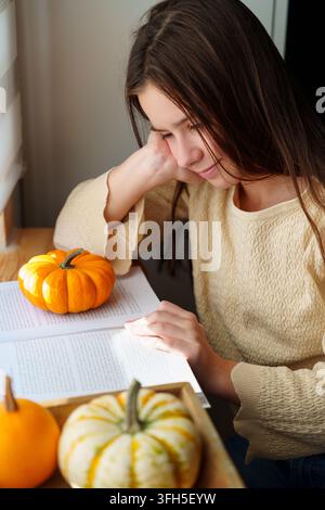 Ragazzina che legge un libro accanto a delle zucche nella calda luce autunnale Foto Stock