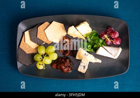 Piatto di formaggi delizioso con uva e cracker assortiti disposti artisticamente Foto Stock