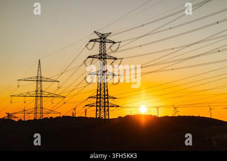 Pali della trasmissione elettrica e turbine eoliche al tramonto Foto Stock