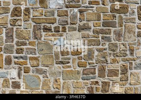 Prima vista, texture a tutto campo di un muro di muratura tradizionale costruito con blocchi di pietra naturale di forma irregolare in varie tonalità terrose Foto Stock