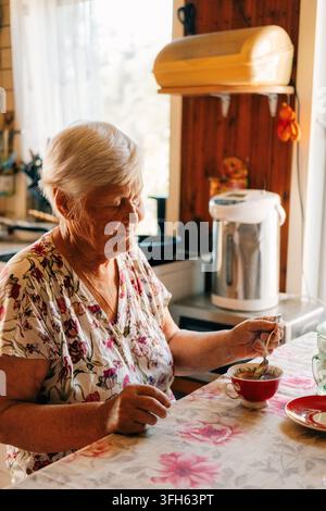 Anziana donna che assapora un dessert in un'accogliente cucina nel pomeriggio Foto Stock