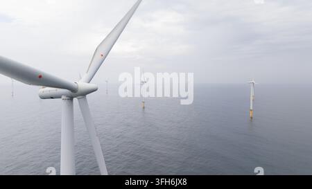 Vista aerea di una fattoria eolica offshore con turbine che si ergono dalle acque calme del mare sotto un cielo nuvoloso, illustrando l'infrastruttura di energia rinnovabile e Foto Stock