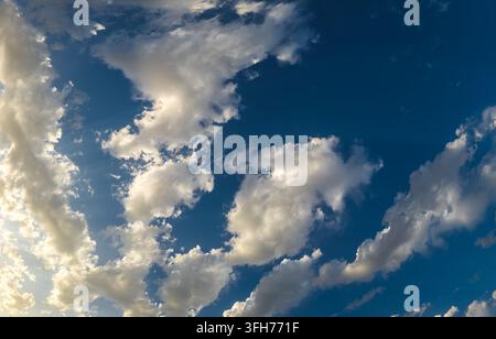 Una vista grandangolare cattura un cielo dinamico pieno di cumuli luminosi. La luce del sole crea un contrasto tra le aree bianche e grigie, enfatizzando la vastità. Foto Stock