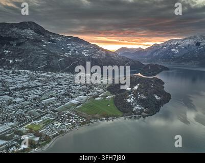 Vista aerea della città di Colico situata sulle rive del Lago di Como con montagne coperte di neve e un cielo al tramonto vibrante a Colico, Lombardia, Italia. Foto Stock
