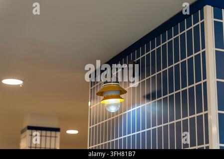 Primo piano di una lampada da parete gialla che illumina un muro piastrellato blu e bianco geometrico in un interno moderno con illuminazione ambientale calda. Foto Stock