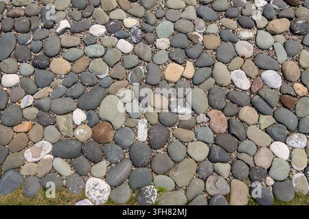 Pietre di fiume lisce e multicolori e ciottoli di varie forme e dimensioni formano un motivo a mosaico naturale denso e texture Foto Stock
