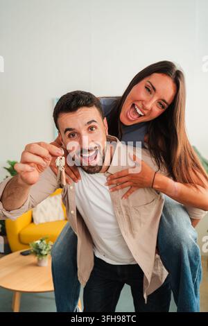 Due amanti gioiosi condividono un momento leggero mentre uno mostra una chiave lucente verso l'obiettivo e l'altro abbraccia da dietro, catturando energia e affetto in Foto Stock