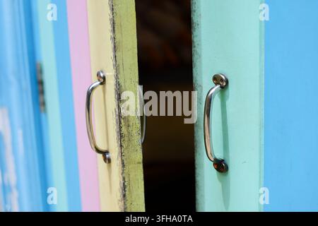 Una porta di legno scolorita e colorata con maniglia in metallo che si apre su un interno scuro, mostra una vernice vibrante, una texture consumata e un design giocoso dell'ingresso residenziale Foto Stock