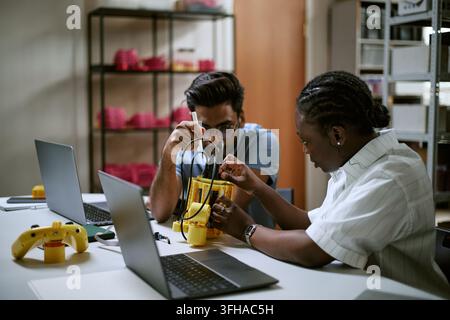 Ingegneri multietnici che assemblano un dispositivo robotico in laboratorio Foto Stock