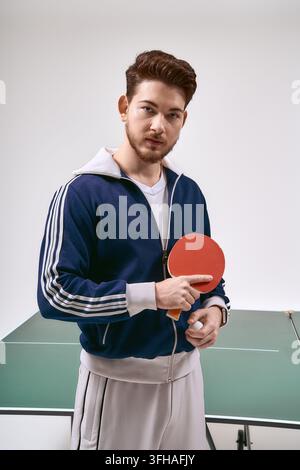 Un giovane uomo affascinante si mostra sicuro di sé, tenendo una racchetta da ping pong, pronto a giocare. Foto Stock
