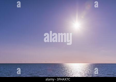 Sole luminoso che splende sull'orizzonte del mare con un cielo viola soffice e spazio per il testo. Foto Stock