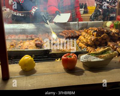 Prima vista di uno stand di street food con una persona che prepara prodotti di carne alla griglia fumanti e sfrigolanti e un hot dog fresco, evidenziando un mercato vivace Foto Stock