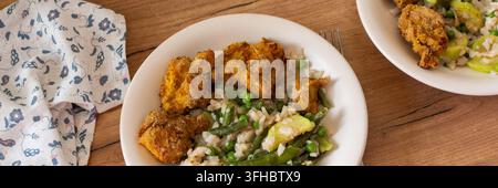 Una ciotola contiene pasta senza glutine con zucchine al forno, piselli e fagiolini insieme a nugget di pollo fritti. Questo pasto è servito su un piano di legno Foto Stock