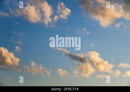 La luce dell'ora dorata illumina soffici nuvole cumulo sparse che fluttuano in un cielo blu sfumato e limpido. Foto Stock