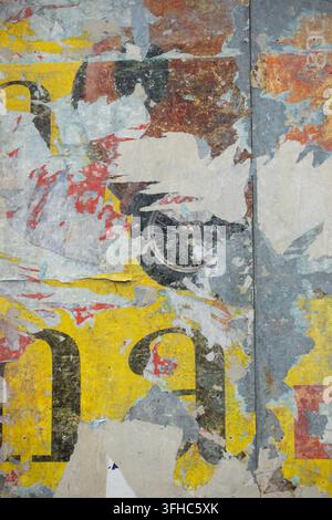 Muro urbano eroso coperto di poster strappati, numeri sbiaditi e texture sovrapposte di carta gialla, blu, grigia e rossa Foto Stock