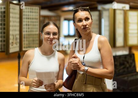 Giovane donna con figlia adolescente cammina lungo un padiglione espositivo, si familiarizza con i manufatti del secolo scorso, oggetti domestici in metallo e legno. Elenco Foto Stock