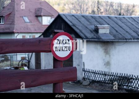 Un cartello stradale circolare rosso e bianco con la scritta ZAKAZ WJAZDU in polacco, che indica il divieto di ingresso, fissato a una barriera in legno resistente che protegge una residenza Foto Stock