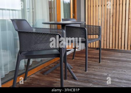 Primo piano di una moderna sistemazione da patio esterno con due sedie in rete nera e un tavolo, ideale per un balcone di hotel o un terrazzo di casa per un tranquillo tempo libero Foto Stock