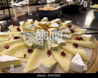 Primo piano di una tavola da formaggio gourmet splendidamente disposta che offre una varietà di formaggi a pasta molle cremosi, formaggi blu aspri e formaggi a pasta dura, perfetti per il servizio a buffet Foto Stock