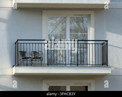 Facciata di appartamento moderno, con balcone nero minimalista, due sedie e grande porta di vetro, che riflette il design residenziale contemporaneo, la vita urbana Foto Stock