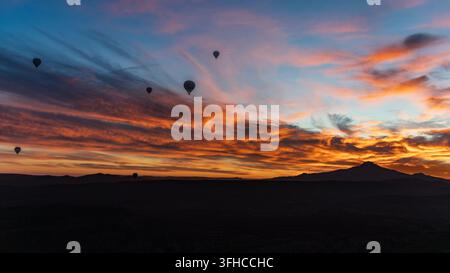 Mongolfiere all'alba sopra la Cappadocia, con il monte Erciyes silouettato sotto nuvole arancioni e rosa, Turchia. Foto Stock