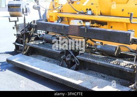Macchine lavorano per spargere asfalto per una nuova strada in un cantiere edile. Foto Stock