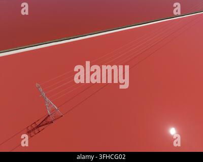 Le linee elettriche si estendono su stagni di sale rosso vivace a Fremont, in California, con il sole che splende intensamente e si riflette sulla superficie dell'acqua Foto Stock