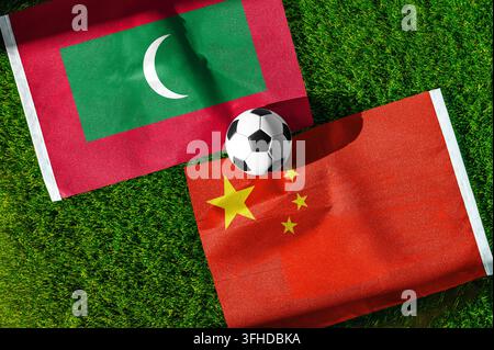 Partita di calcio Maldive vs. Cina. Bandiere nazionali sull'erba verde con un pallone da calcio al centro. Sfondo di calcio per una partita internazionale. Foto Stock