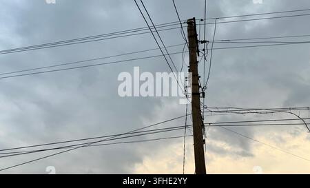 Palo di servizio e cavi aerei silouettati contro un cielo nuvoloso, creando una scena minimalista di infrastruttura urbana con ampio spazio per il testo. Foto Stock