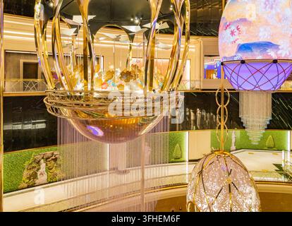 Grandi sfere dorate decorative con intricate lavorazioni metalliche e strasi pendenti illuminano l'interno su più livelli di un centro commerciale moderno. Foto Stock