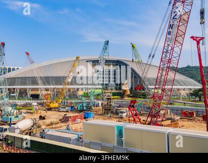 Macao, Cina, 16 apr. 2024 - Diverse gru di costruzione colorate dominano il cantiere attivo davanti a una massiccia struttura architettonica moderna Foto Stock
