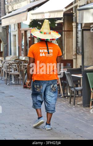 Uomo nero con maglietta arancione e sombrero alto che cammina lungo una strada stretta nel quartiere vecchio di Tours, Indre-et-Loire (37), Francia. Foto Stock