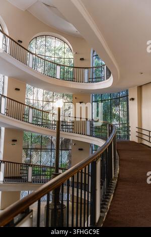 Una vista dall'alto di una elegante scala a chiocciola curva all'interno di un edificio storico. La struttura presenta più livelli con ringhiere in metallo scuro, woo Foto Stock