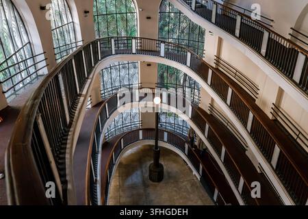 Una vista dall'alto di una elegante scala a chiocciola curva all'interno di un edificio storico. La struttura presenta più livelli con ringhiere in metallo scuro, woo Foto Stock