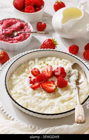 Riso al latte tradizionale tedesco con riso al latte e fragole fresche, lamponi interi e purea di frutti rossi dolce servita su uno sfondo di marmo, vertica Foto Stock
