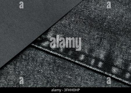 Carta grigio scuro che si sovrappone a una tasca di jeans scuro con bordi cuciti e una divisione diagonale dello sfondo Foto Stock