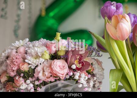Eccellenti composizioni floreali con vibranti orchidee rosa e rose delicate esposte vicino a tulipani colorati, offrendo uno sfondo stagionale gioioso per spec… Foto Stock