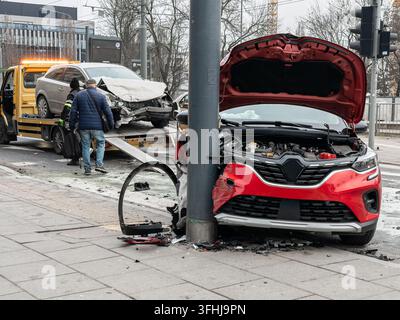 Il veicolo rosso è fermo con il cofano aperto dopo una collisione contro il palo, mentre una persona del servizio gestisce la scena vicino a un camion di carico che contiene Foto Stock