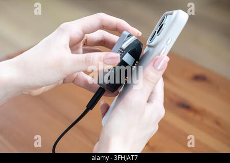 Le mani collegano un'unità SSD esterna a un telefono cellulare, illustrando come l'hardware portatile semplifica la gestione dello storage e la produttività durante un periodo impegnato Foto Stock