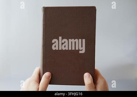 Un vecchio libro con copertina marrone senza titolo tenuto da due mani, primo piano. Antica legge, verità bibliche Foto Stock