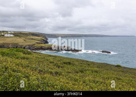 Vista su una penisola costiera con onde che si infrangono su scogliere rocciose e colline erbose Foto Stock